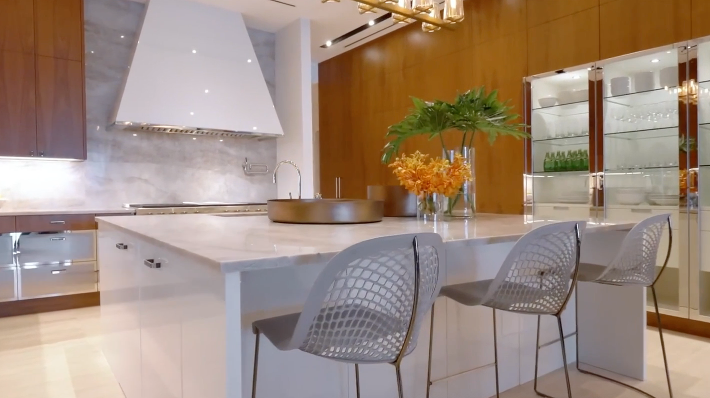 A kitchen with a large island and stools and a vase of flowers on the counter.