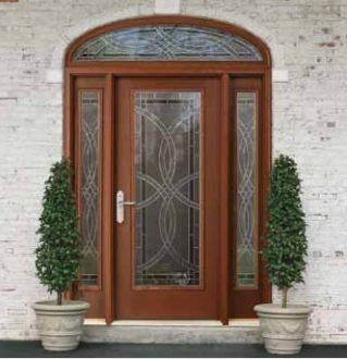 Wooden front door with glass panels and sidelights, flanked by potted evergreen trees.