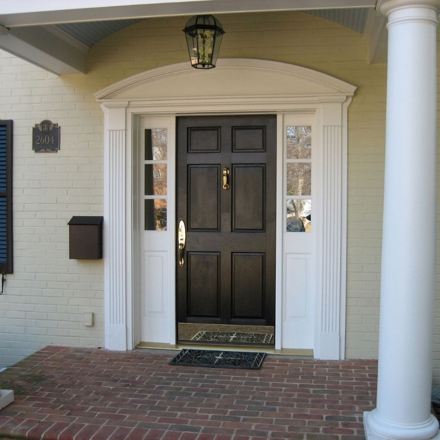 Black front door with sidelights, under a porch, surrounded by white trim, set on brick.
