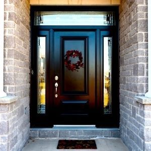 Black front door with sidelights and a transom window, set in a brick facade, decorated with a wreath.