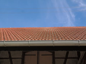 A red tiled roof with a white gutter and a blue sky in the background.