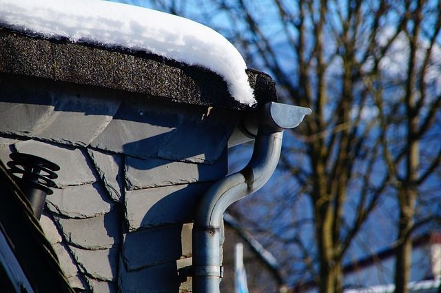A close up of a gutter on a roof with snow on it.