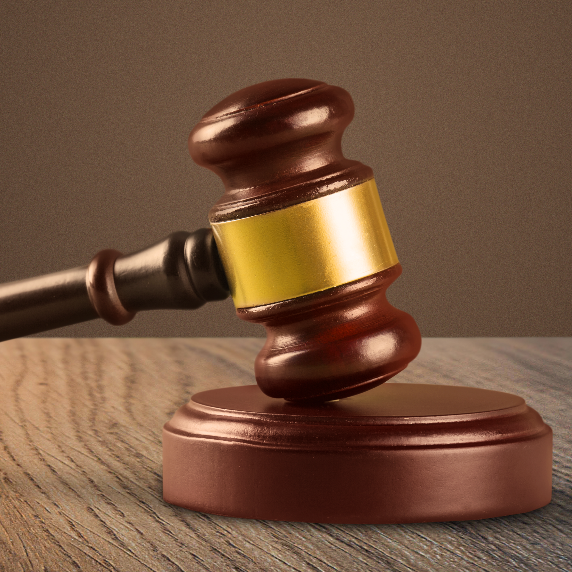 Brown and gold gavel on a wooden surface with a brown background.