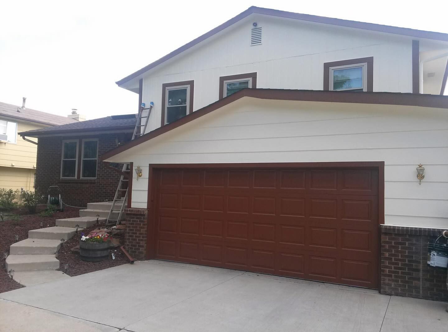 A white house with a brown garage door and stairs