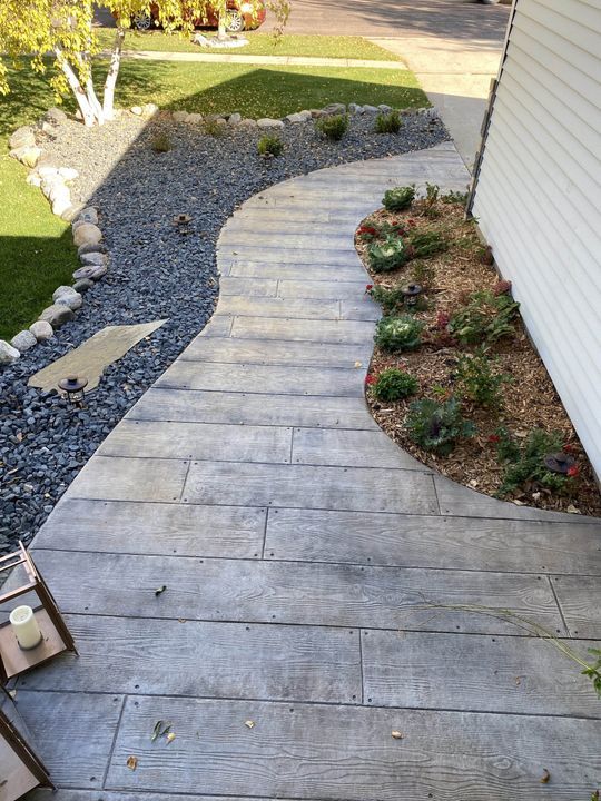 A wooden walkway leading to a house with rocks and plants.