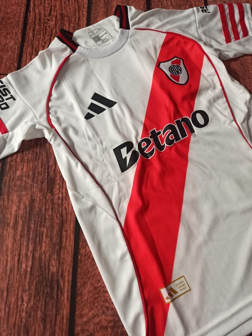 Camiseta de fútbol blanca con franja y acentos rojos; logotipo de Betano, logotipo de Adidas, escudo de River Plate.