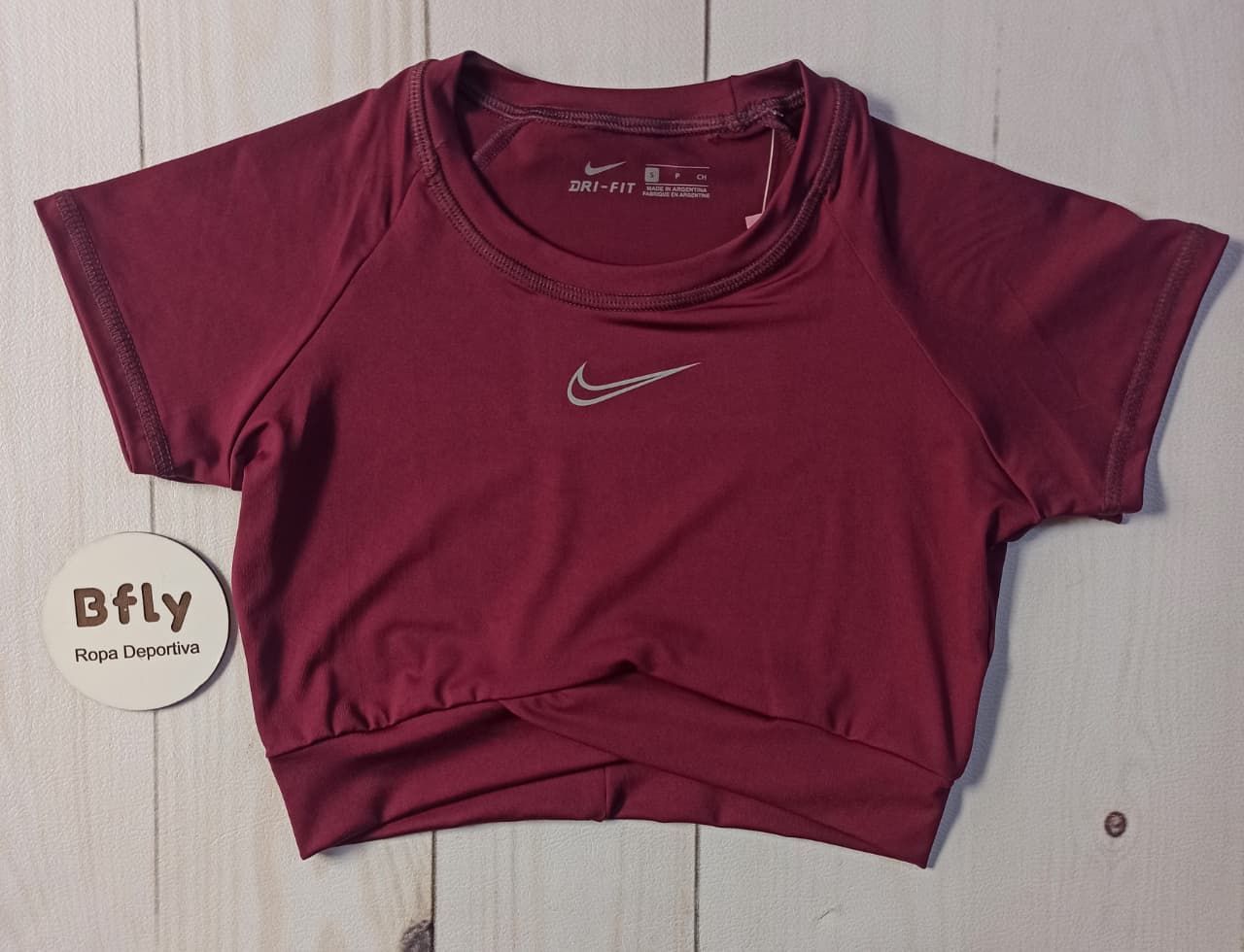 Tres crop tops de Nike, de color rosa, marrón y burdeos, sobre una superficie de madera blanca.
