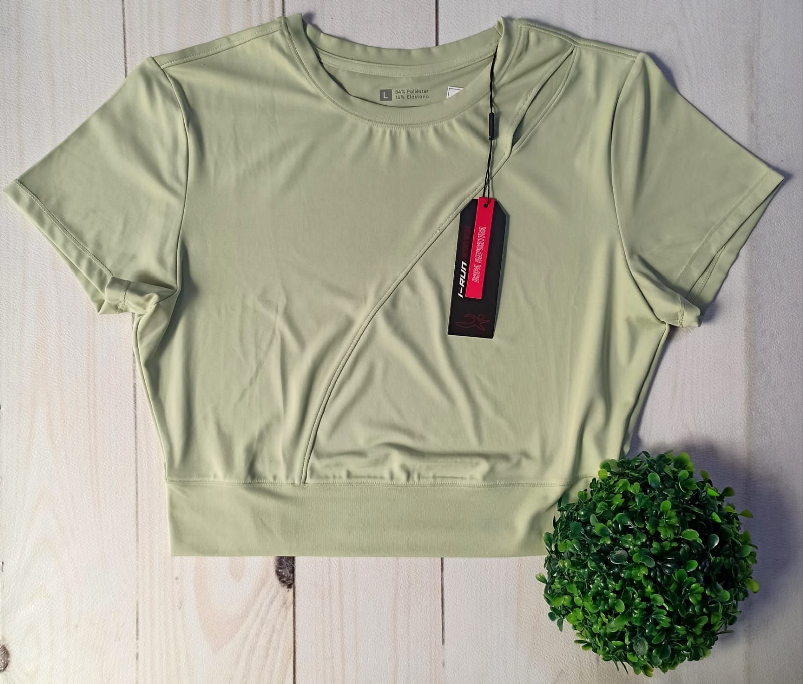 Tres camisetas deportivas de manga corta: melocotón, azul y verde; dispuestas sobre una superficie con vetas de madera.