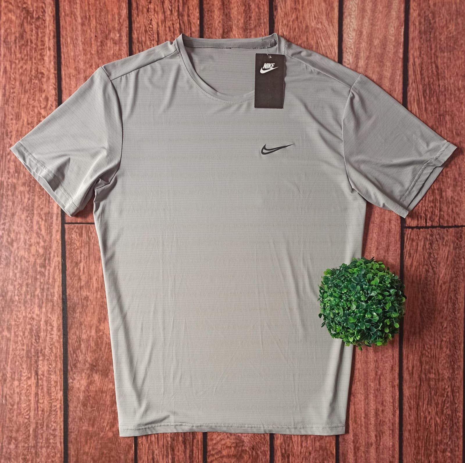 Camiseta Nike gris con el logo de Nike sobre fondo de madera junto a una pequeña planta verde.