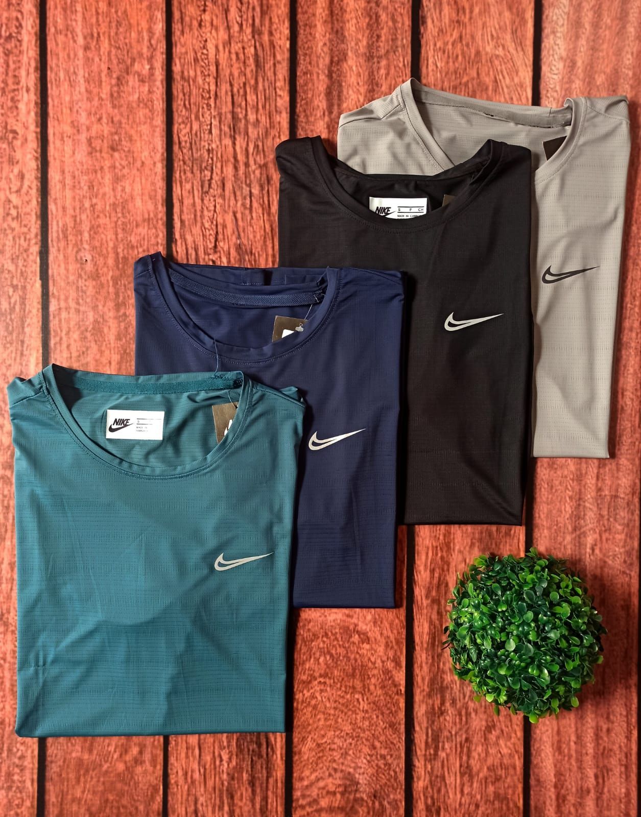 Camiseta Nike gris con el logo de Nike sobre fondo de madera junto a una pequeña planta verde.