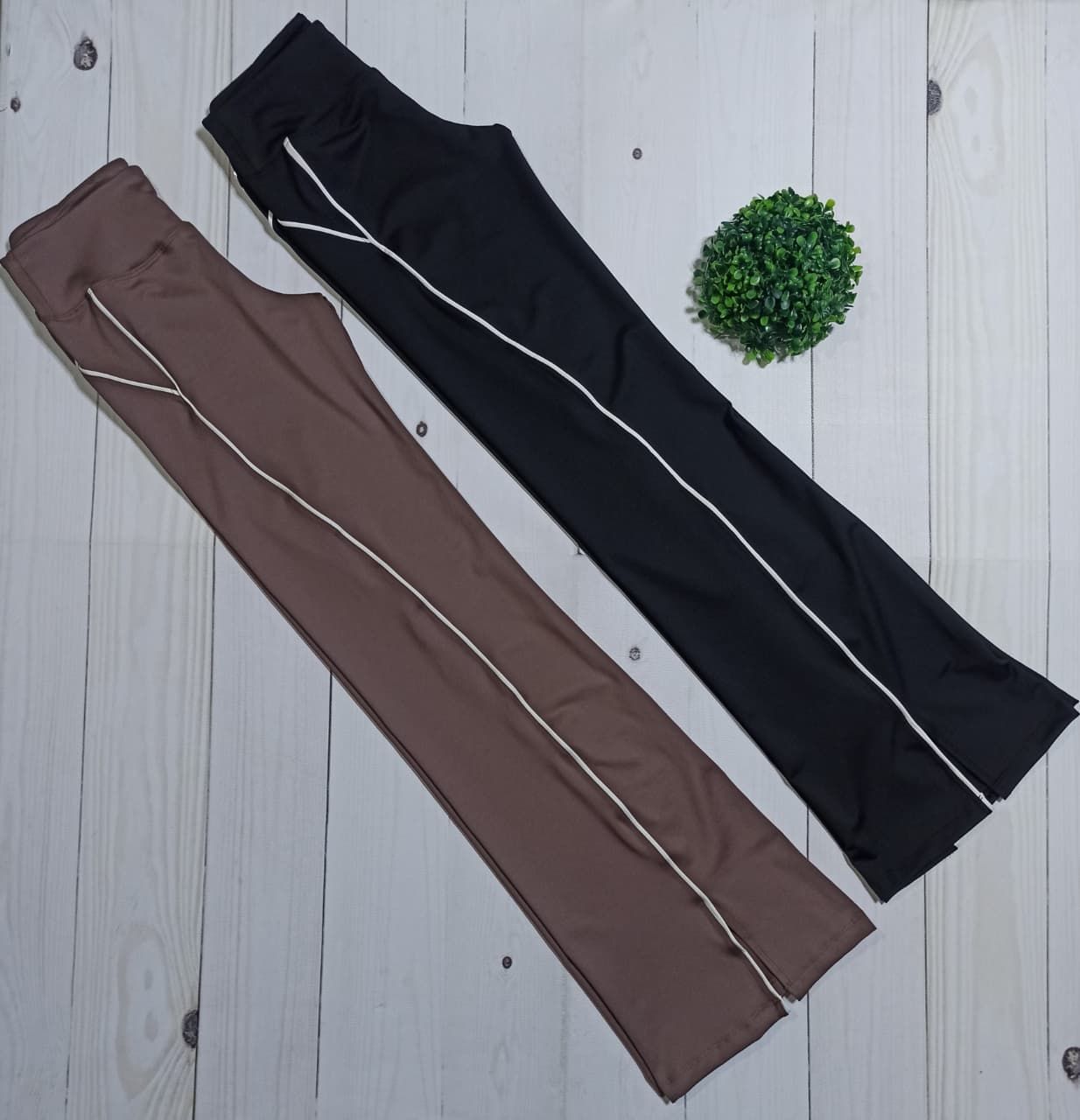 Dos pantalones deportivos, de color marrón y negro, con ribetes blancos, sobre una superficie de madera.
