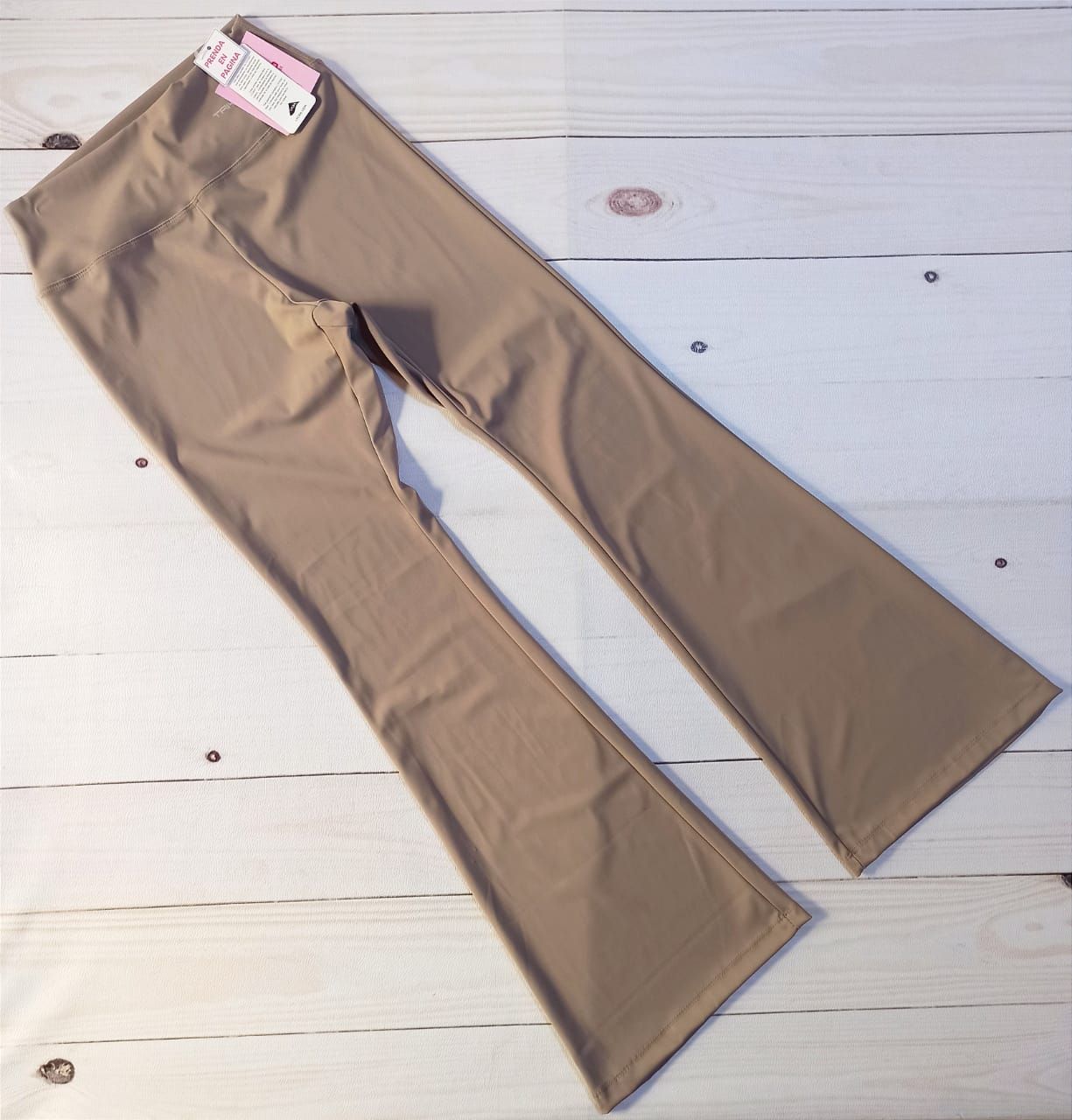 Leggings beige acampanados sobre fondo de madera clara. Etiqueta adjunta.