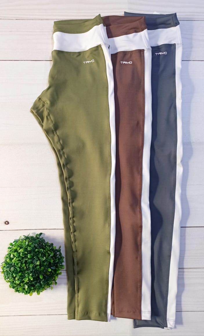 Mujer con leggings color oliva con raya lateral blanca, sujetador deportivo blanco y zapatillas blancas.