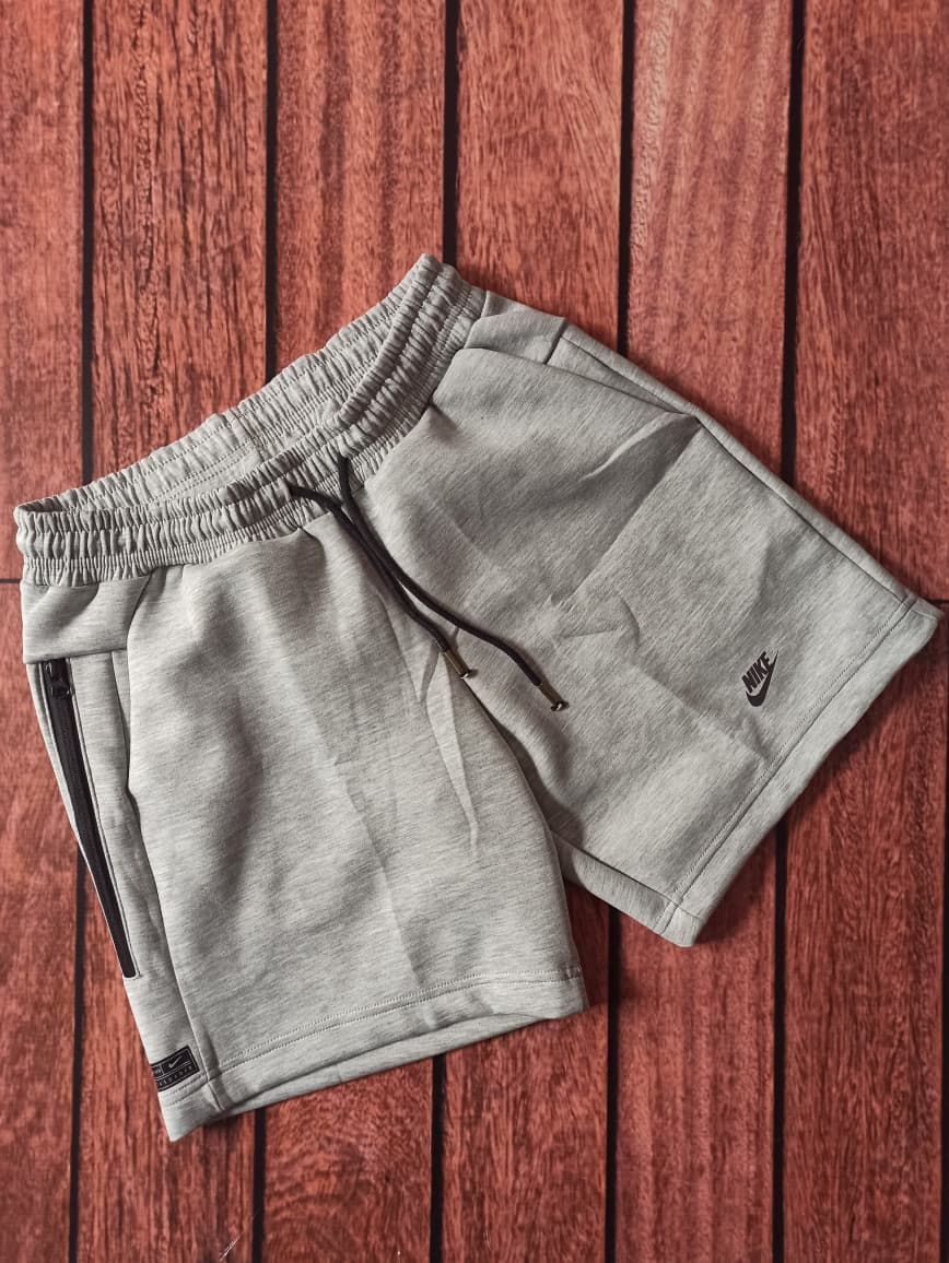 Tres pares de pantalones cortos Nike en negro, gris y gris claro apilados sobre una superficie de madera.