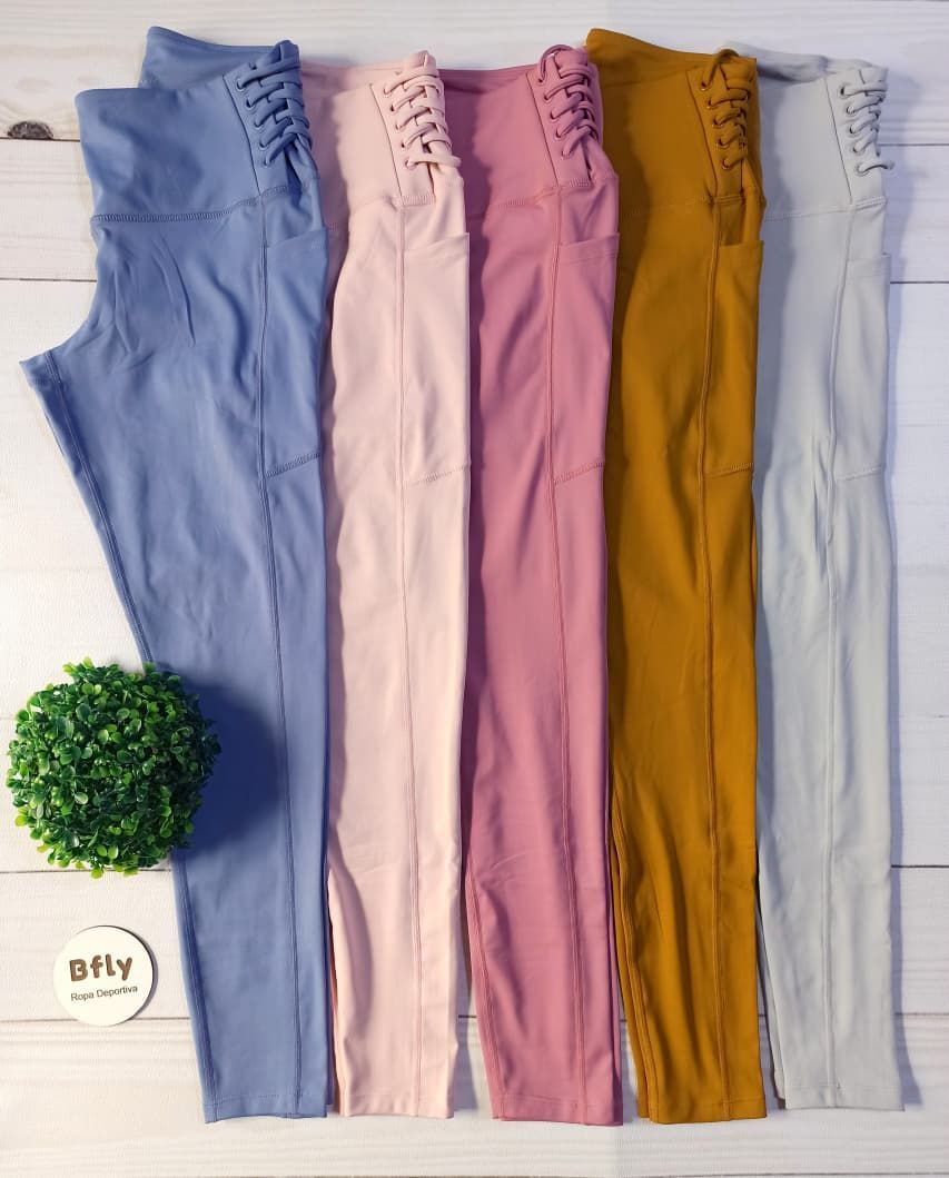 Leggings rosas de cintura alta con bolsillos laterales, sobre un fondo de madera junto a una planta verde.