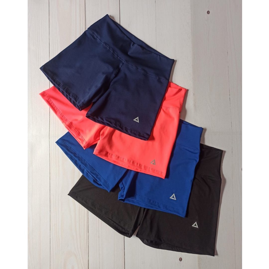 Mujer con sujetador deportivo azul y pantalones cortos posa con las manos en las caderas.