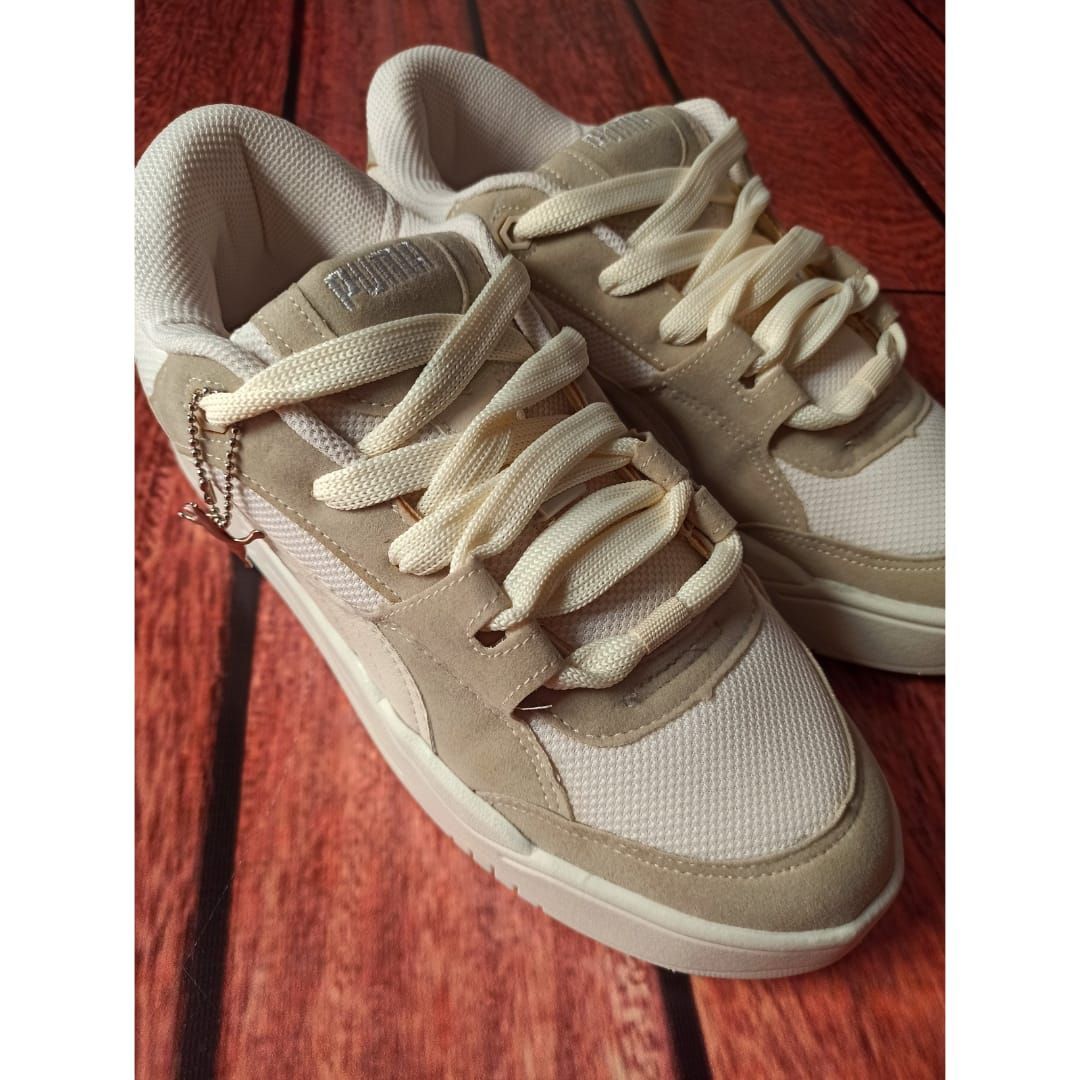 Un par de zapatillas deportivas color beige sobre un suelo de madera rojiza, vistas desde arriba.