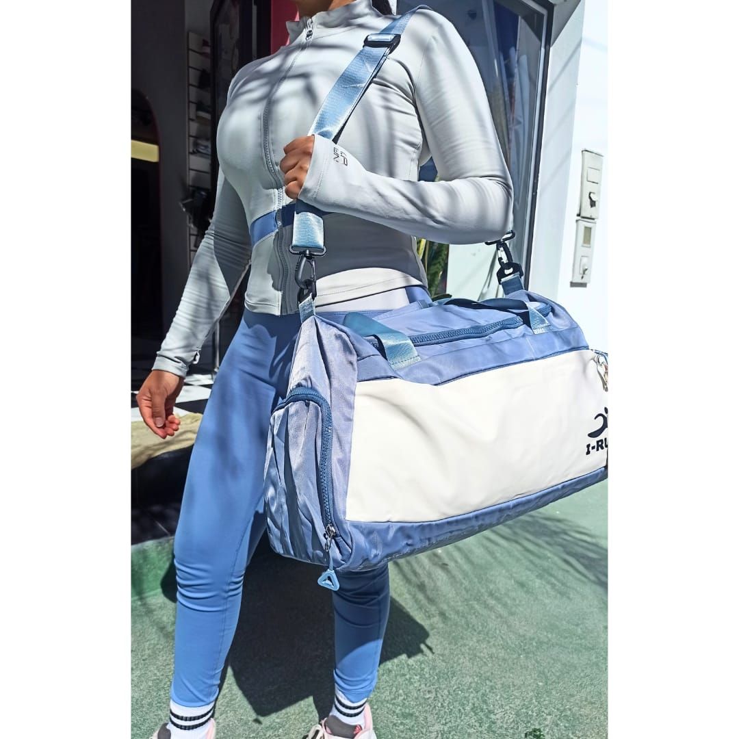 Mujer con ropa deportiva sosteniendo una bolsa de lona azul y blanca, parada afuera.