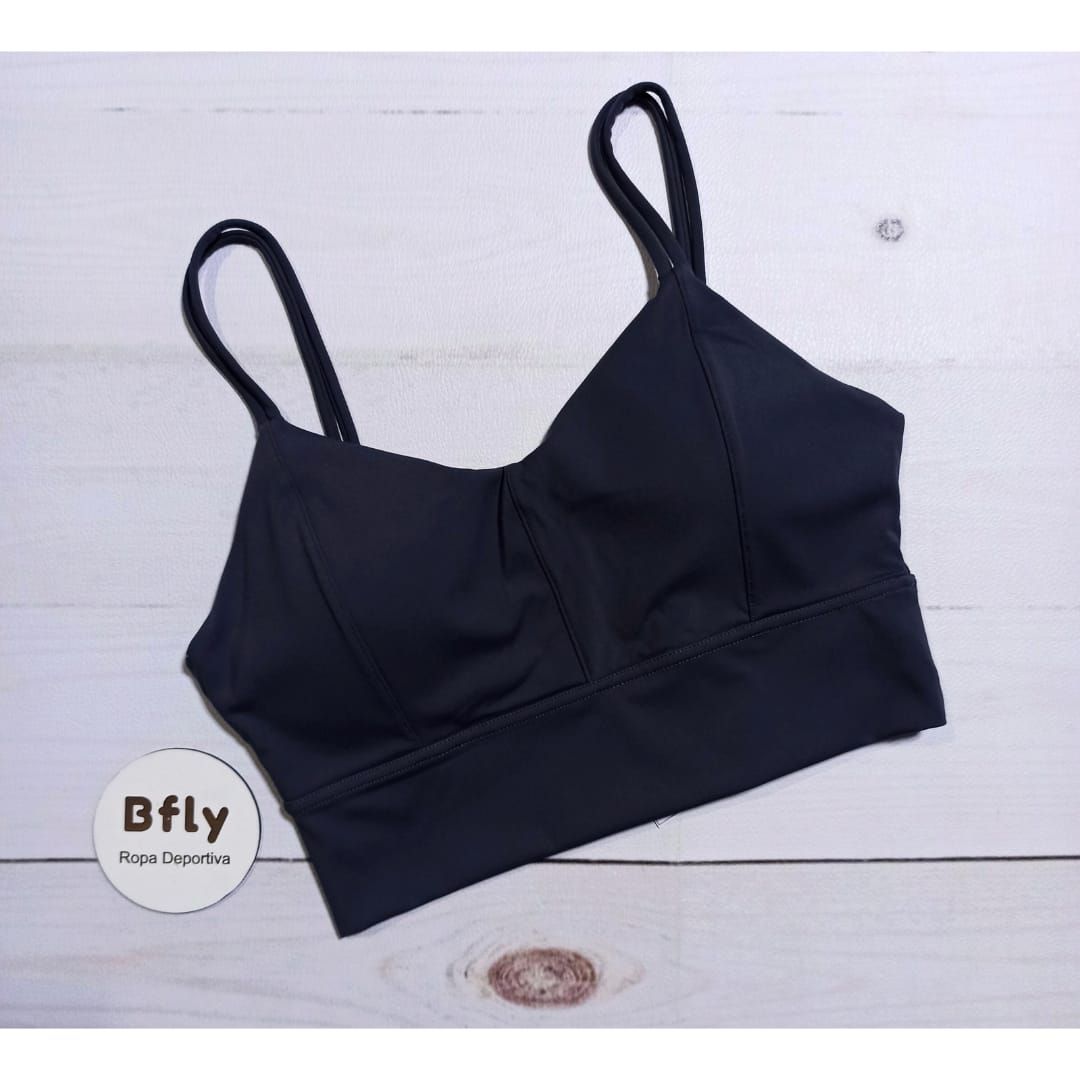 Mujer en ropa deportiva posando en un gimnasio. Lleva un sujetador deportivo verde y mallas, mirando hacia otro lado.