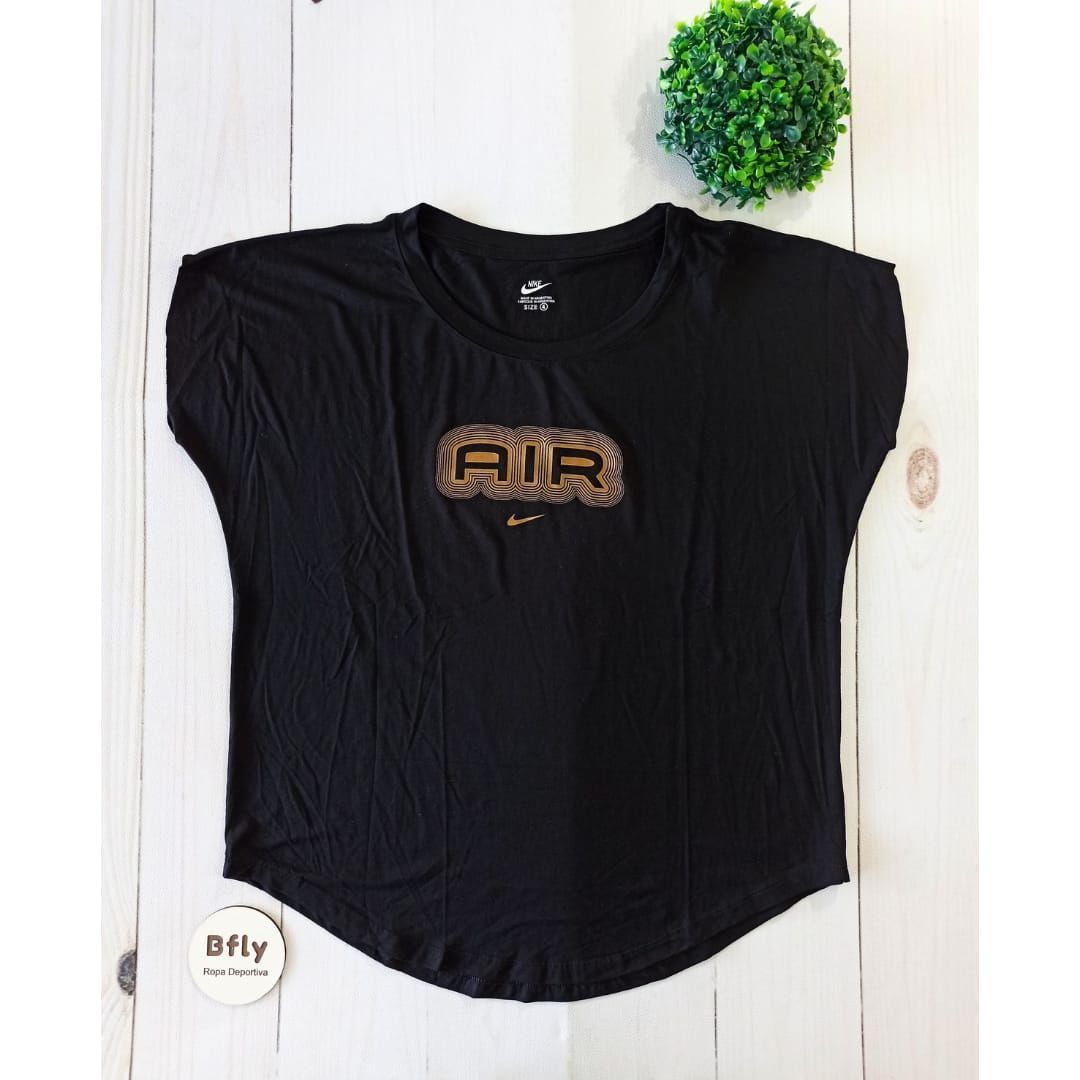 Mujer con camiseta Nike coral y leggings grises. Logotipo de Nike visible. Interior, junto a una ventana.