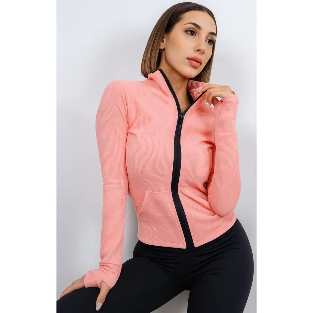 Mujer que lleva una chaqueta con cremallera de color melocotón con ribete negro y leggings negros.