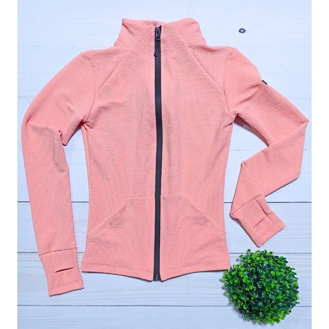 Mujer que lleva una chaqueta con cremallera de color melocotón con ribete negro y leggings negros.