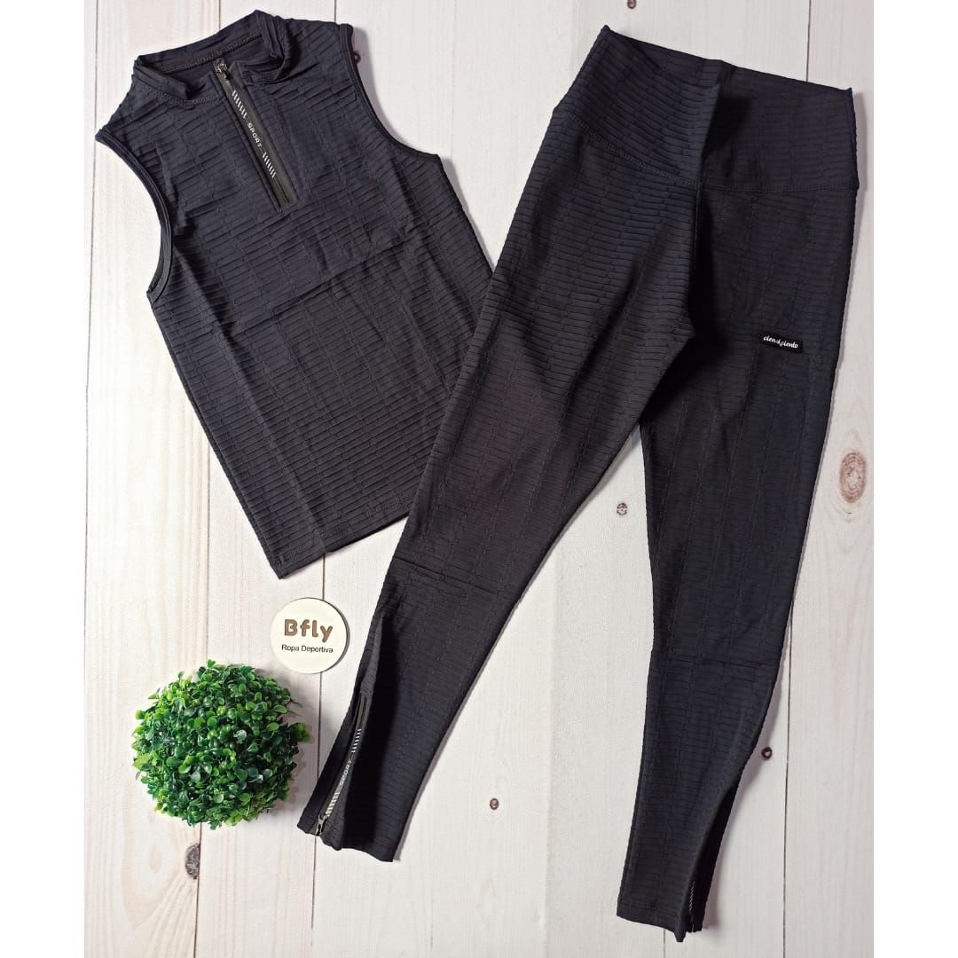 Mujer vestida con un mono deportivo azul marino y zapatillas negras, posando frente a una pared blanca.