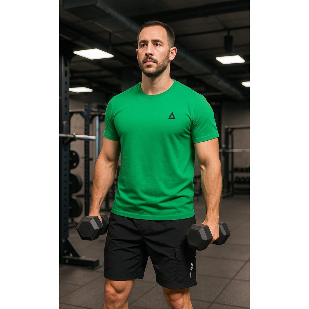 Hombre con camisa verde y pantalones cortos negros sosteniendo mancuernas en un gimnasio.