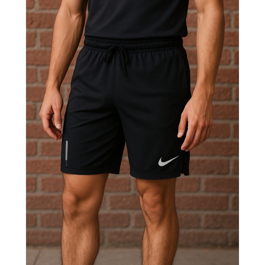 Hombre vestido con pantalones cortos y camiseta deportiva negra, de pie frente a una pared de ladrillos.