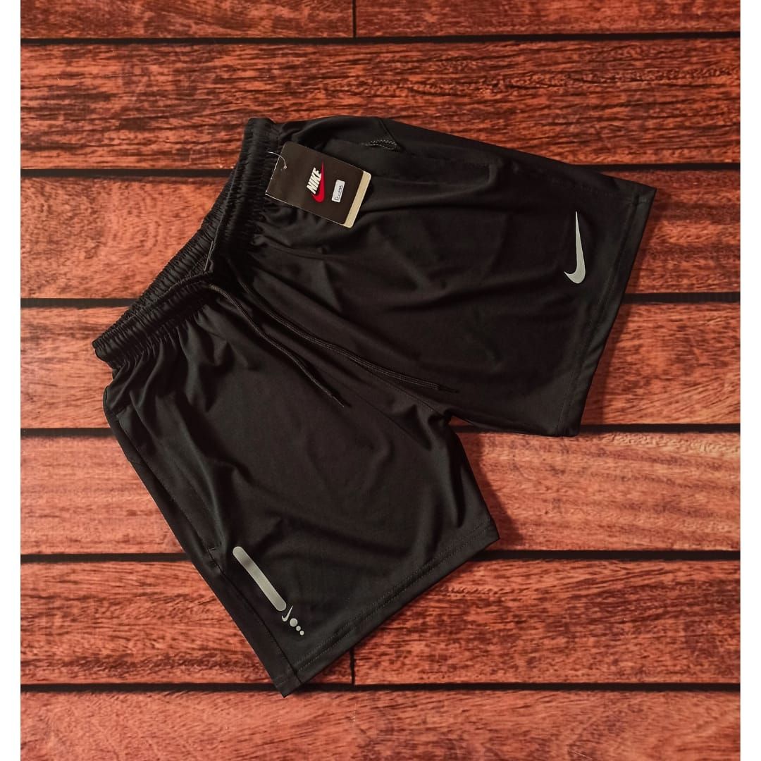 Hombre vestido con pantalones cortos y camiseta deportiva negra, de pie frente a una pared de ladrillos.