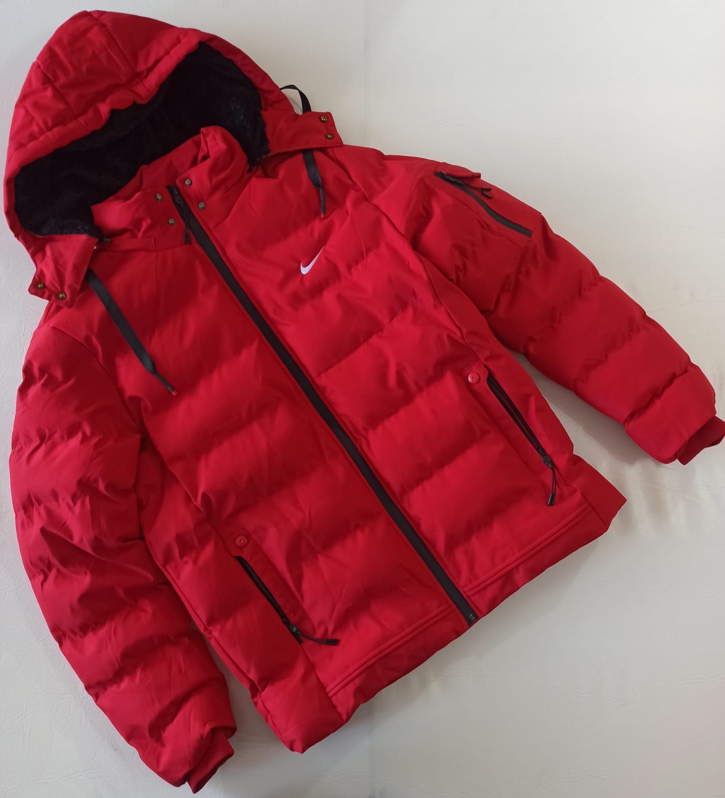 Chaqueta acolchada roja con capucha extendida sobre un fondo blanco.