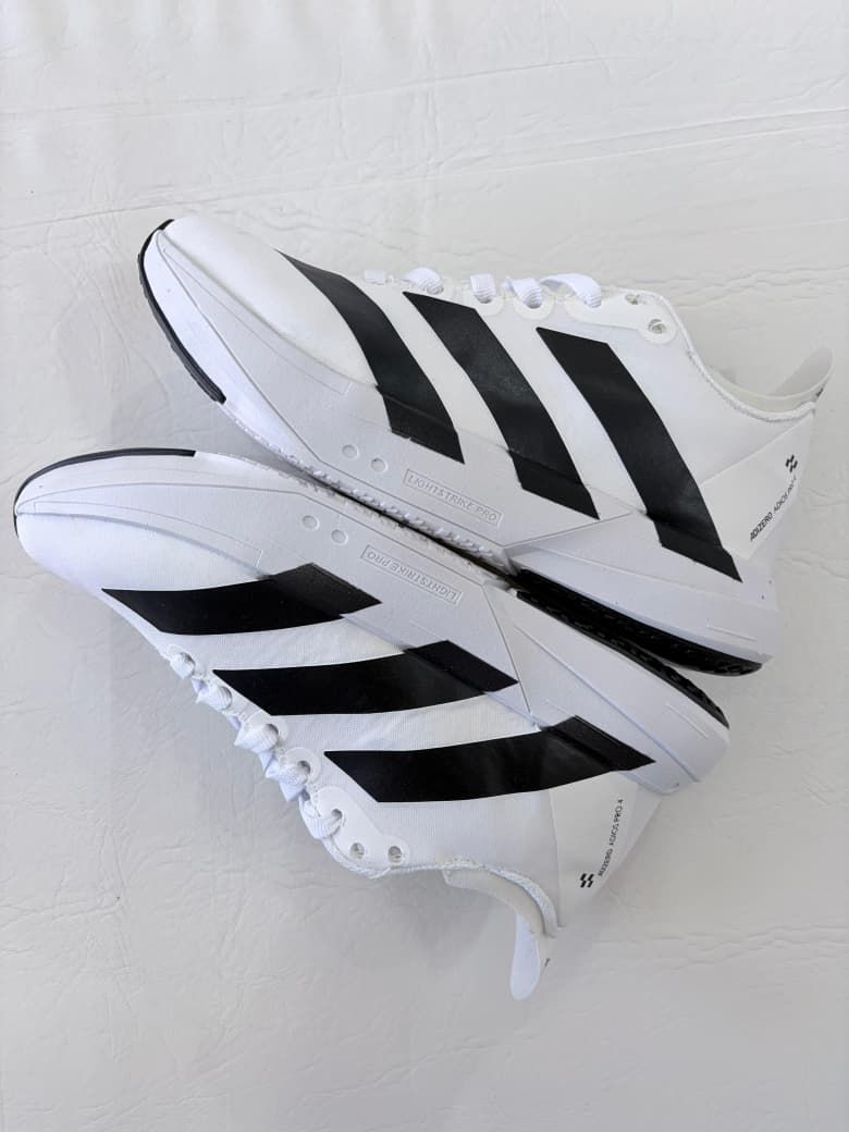 Zapatillas deportivas altas blancas de Adidas con rayas negras, apiladas sobre un fondo blanco.