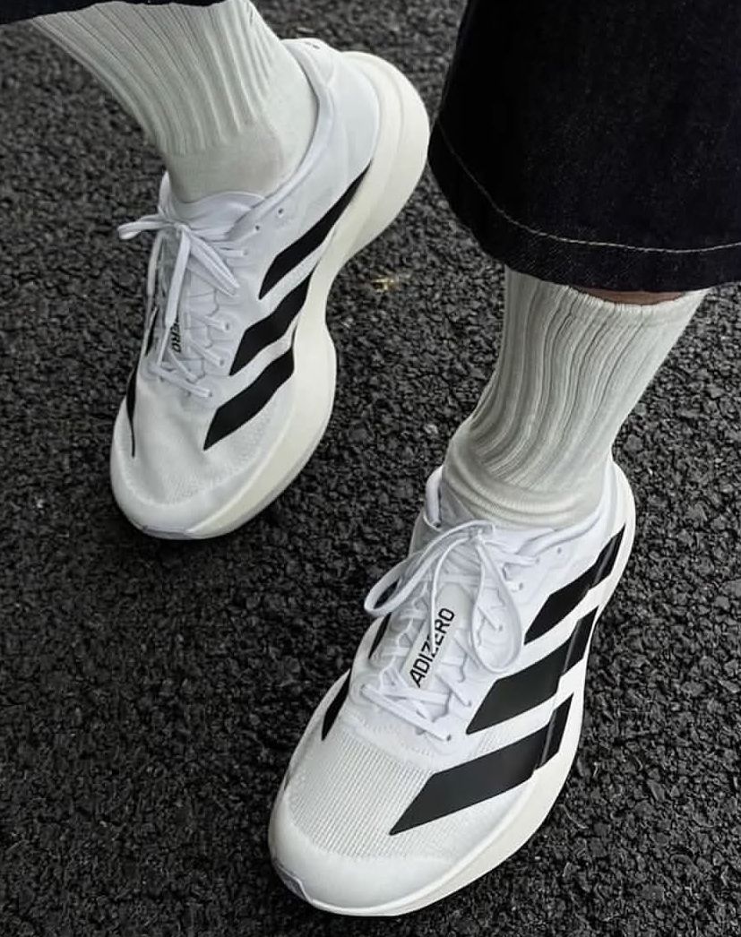 Zapatillas deportivas altas blancas de Adidas con rayas negras, apiladas sobre un fondo blanco.