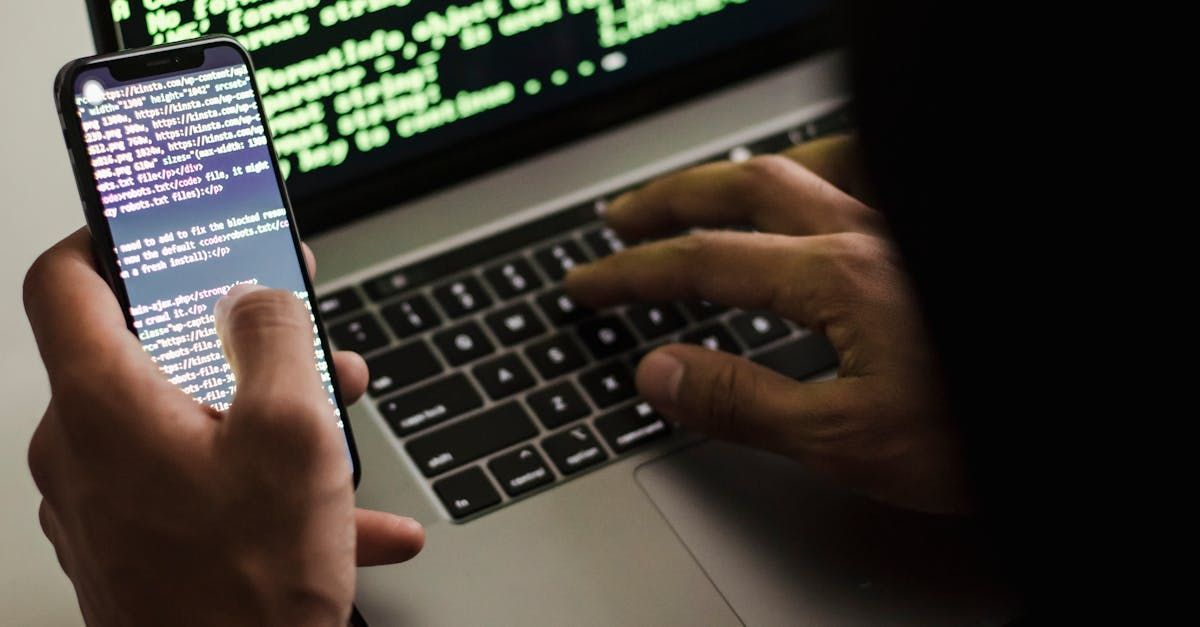 Eine Person tippt auf einem Laptop, während sie ein Mobiltelefon hält - Illustration Informationssicherheit