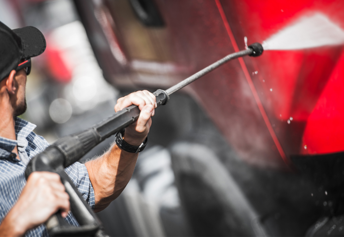 A man is cleaning a red truck with a high pressure washer.