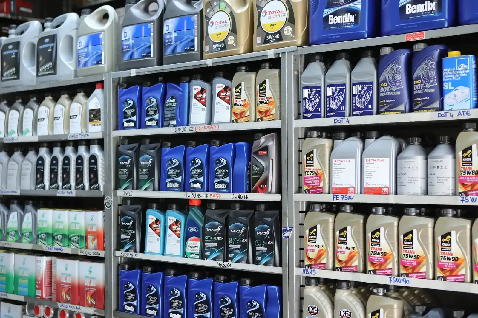 Scaffali pieni di vari contenitori di olio motore in un ambiente da negozio.