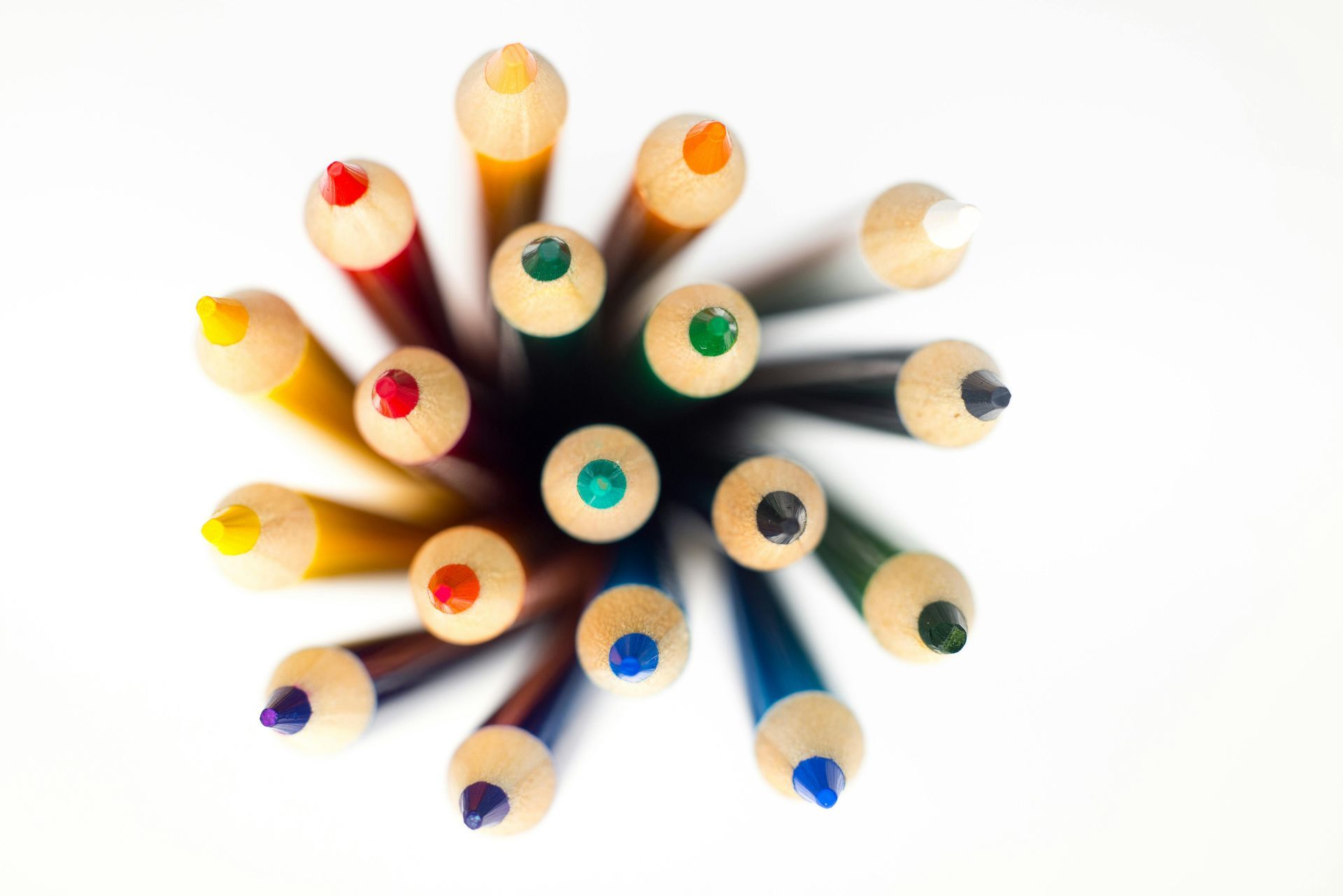 Overhead shot of colorful colored pencils, tips facing up against a white background.