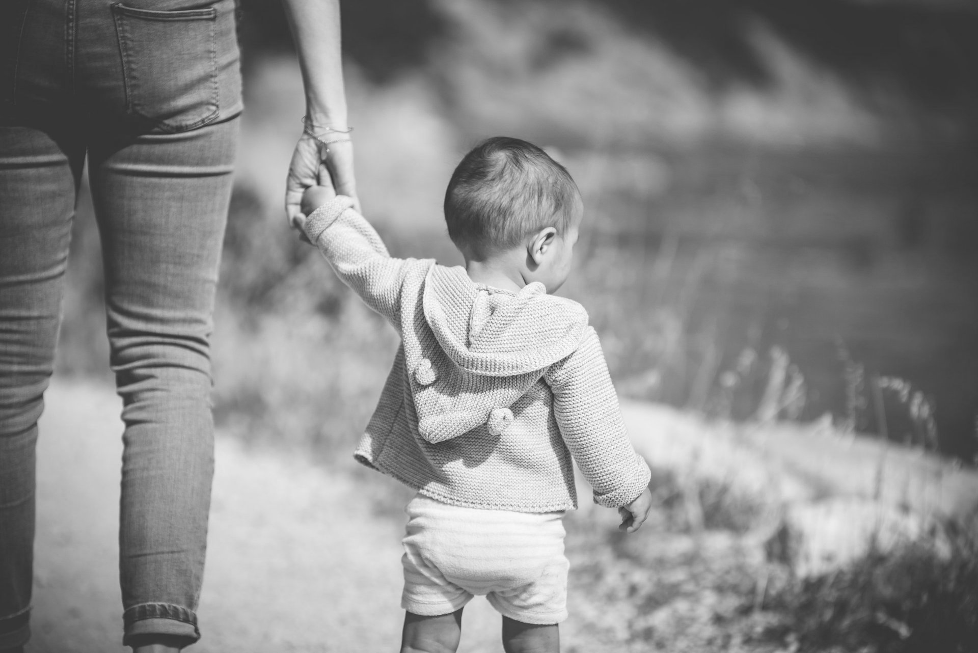 Child holding adult's hand, walking outdoors. Black and white photo.