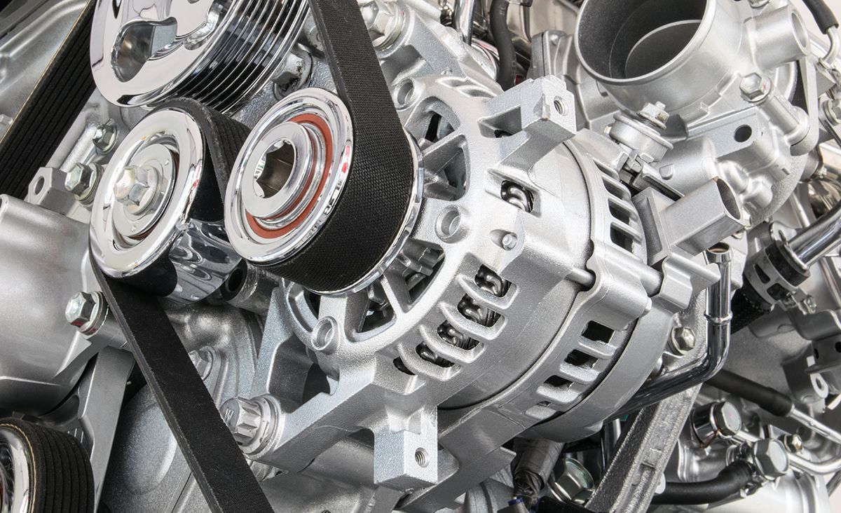Close-up of a car engine with belts, pulleys, and alternator, various metallic components.