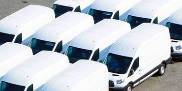 A row of white vans are parked in a parking lot.