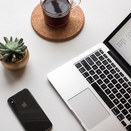 A laptop is open on a table next to a phone and a cup of coffee