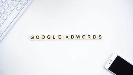 The word google adwords is written on a white surface next to a keyboard and a cell phone.