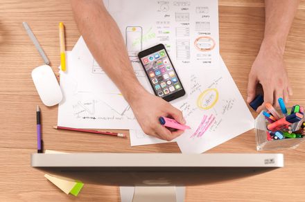 A person is sitting at a desk with a computer and a cell phone.