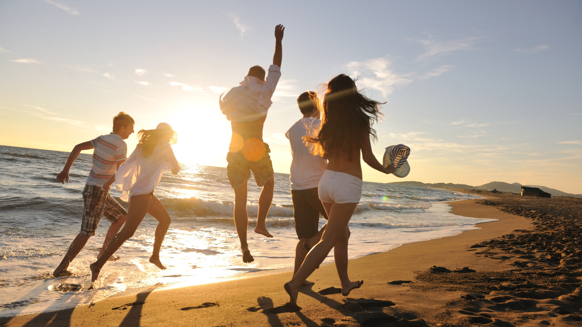 A group of people are jumping in the air on the beach at sunset.