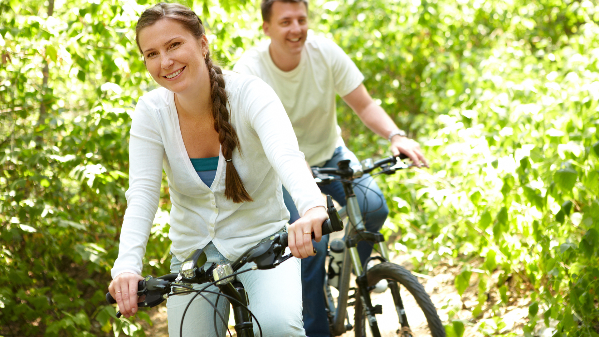 A man and a woman are riding bicycles in the woods.