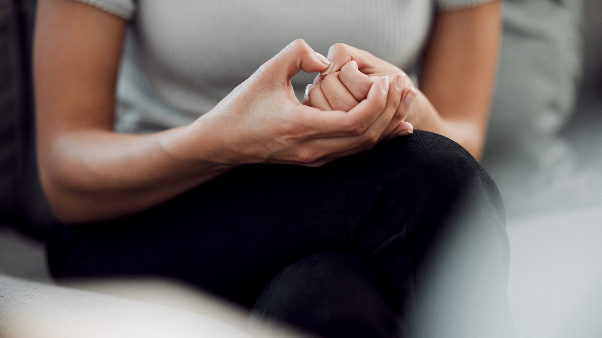 A woman is sitting on a couch with her hands folded in a heart shape.