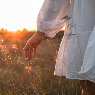 A woman in a white dress is standing in a field of tall grass.