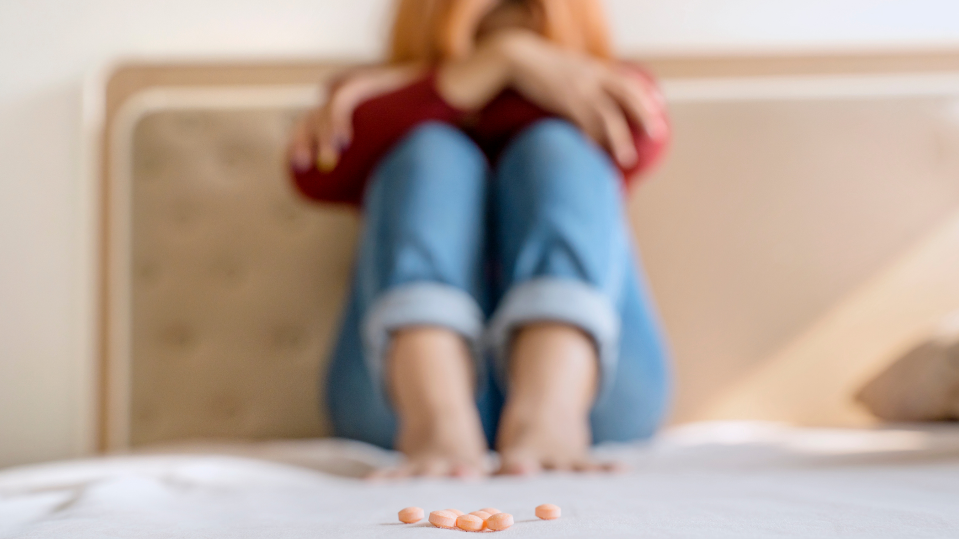 A woman is sitting on a bed with her legs crossed and pills on the bed.