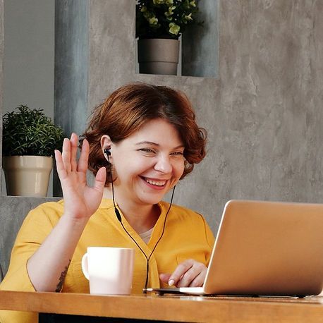 A woman in a yellow shirt is sitting at a table with a laptop and headphones on.