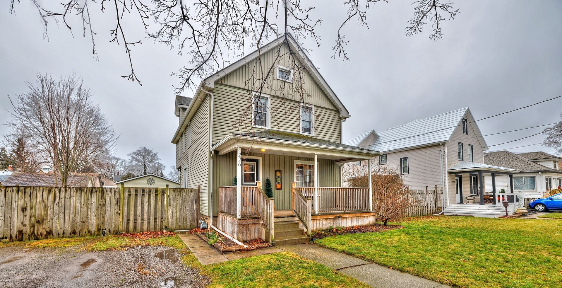 A green two-storey house with a front porch and a two-car private driveway.